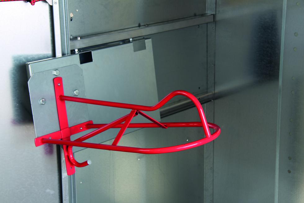 Ein ausziehbarer und ausgezogener Sattelhalter, auf der Innenseite einer verzinkten Seitenwand eines Sattelschranks befestigt, rotes Auflagegestänge mit kleinem Haken auf der Unterseite
