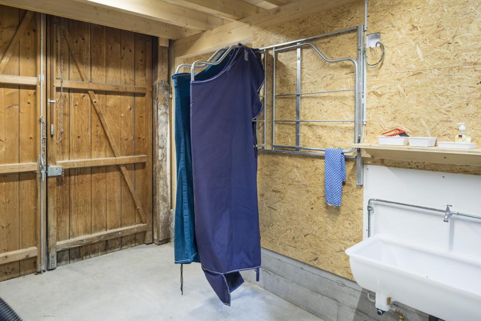 ein Deckenhalter mit sechs Aufhängungen an Sperrholzwand montiert, metallic Rohrgestänge, behängt mit zwei Decken, blau und cyan, vorderste Aufhängung eingeklappt Ansicht von der Seite